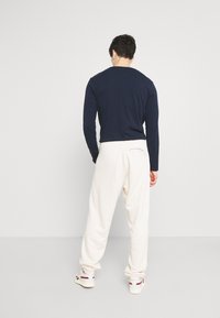 Marinblå långärmad skjorta i kombination med krämfärgade sweatpants. Outfiten har en avslappnad passform, enkla texturer och ett lätt tyg. Sneakers ingår.