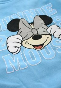 Sweatshirt bleu clair avec un personnage de dessin animé portant un nœud gris couvrant ses yeux. Le texte indique « MINNIE MOUSE » en lettres blanches grasses.