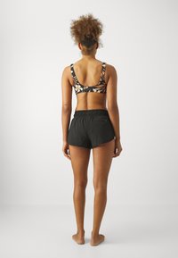 Sportliche schwarze Shorts kombiniert mit einem mehrfarbigen, floralem Sport-BH. Weicher Stoff, lässige Passform und elastischer Bund mit einer kleinen Gesäßtasche.