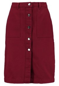 Falda de mezclilla burdeos con una cintura ajustada, cierre frontal de botones y dos bolsillos tipo parche. Presenta un dobladillo recto y una tela texturizada.