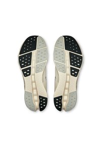 Semelles de chaussures disposées de manière symétrique avec des sections noires, grises et crème. Motifs texturés et perforations pour une meilleure adhérence et flexibilité.