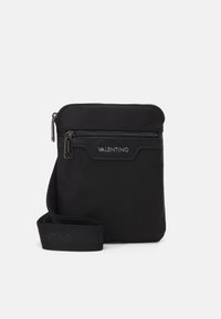 Sac bandoulière en nylon noir avec fermeture éclair, présentant une texture lisse et une bandoulière estampillée. Design compact idéal pour les essentiels.