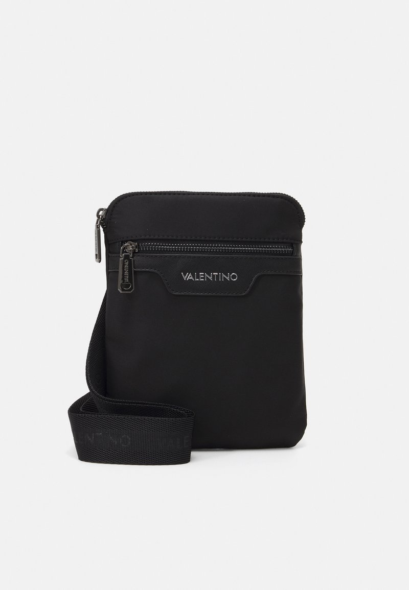 Sac bandoulière en nylon noir avec fermeture éclair, présentant une texture lisse et une bandoulière estampillée. Design compact idéal pour les essentiels.