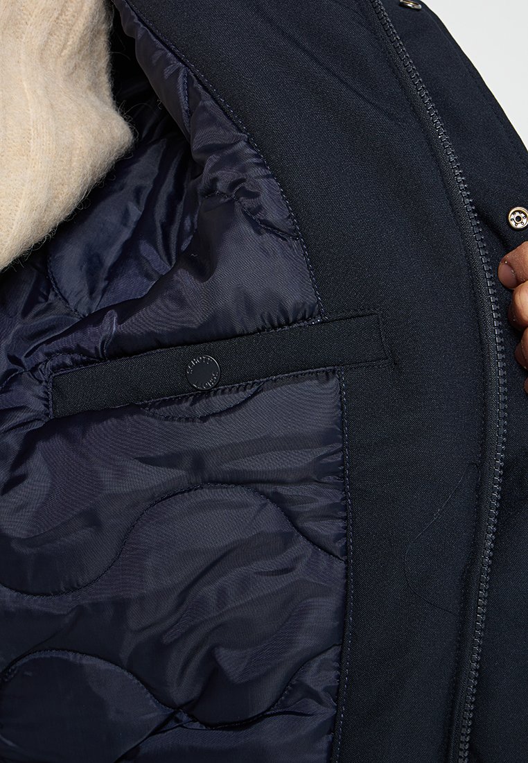Veste marine avec doublure matelassée, dotée d'une poche verticale fermée par un bouton-pression et d'une texture lisse.