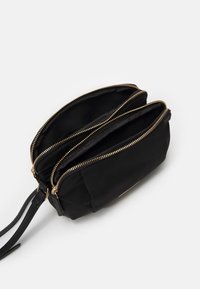 Pochette da polso nera con due scomparti aperti con cerniere e cerniere color oro su sfondo bianco.
