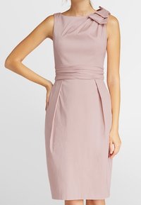 Robe ajustée rose clair avec une jupe plissée, sans manches, et une accent en nœud sur l'épaule, fabriquée en tissu doux.