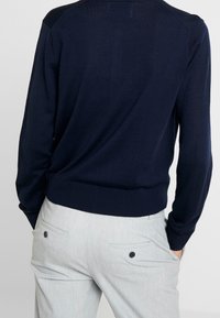 Maglione lavorato a maglia blu navy con orlo e polsini a costine, caratterizzato da un design semplice e una texture liscia. Abbinato a pantaloni grigio chiaro con tasche.