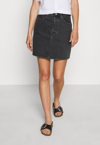 Falda de mezclilla en gris oscuro, con cinco bolsillos, de corte midi y una ligera forma en A. Combinada con sandalias negras tipo slide.