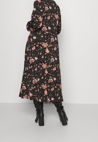 Mekko, jossa on musta pohja ja oransseja sekä vaaleanpunaisia kukkia, pitkät hihat ja liehuva helma. Yhdistetty polven ylle ulottuviin mustiin korkokenkiin.