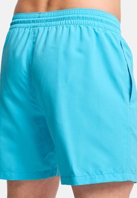 Μπλε μαγιό από ελαφρύ ύφασμα, με ελαστική μέση και πλαϊνές τσέπες. Λείο υφή με σχέδιο σε μονόχρωμο.