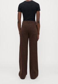 Personne portant un pantalon large marron taille haute avec un imprimé léopard subtil et un haut noir près du corps à manches courtes, vue de dos.