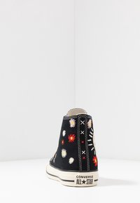 Černé plátěné kotníkové tenisky s multikulturními květinovými vyšíváním a kontrastním stehem. Mají gumovou podrážku a branding na patě.