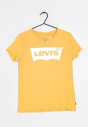 Żółta koszulka Levi's z krótkim rękawem i białym logo nadrukowanym na piersi, wisząca na czarnym wieszaku na białym tle.