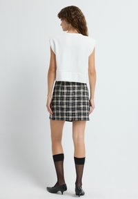 Top blanco corto con diseño estructurado en los hombros, combinado con una falda corta de cuadros en blanco y negro, medias altas negras y tacones negros.