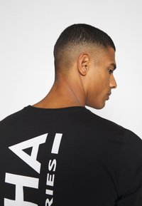 Schwarzes Baumwoll-T-Shirt mit einem großen weißen Text-Graphic auf der Rückseite. Rundhalsausschnitt-Design mit kurzen Ärmeln, glatte Textur.