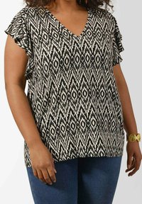 Black and white patterned top with a V-neck design and ruffled sleeves, made of lightweight fabric. Paired with denim jeans.
