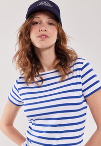 Witte t-shirt met blauwe horizontale strepen, voorzien van een ronde halslijn en korte mouwen, gecombineerd met een marineblauwe ribfluwelen pet.