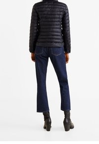 Czarna puchowa kurtka z poziomym przeszyciem, niebieskie dżinsy o lekko rozszerzanym kroju i czarne botki na obcasie, widziane z tyłu.