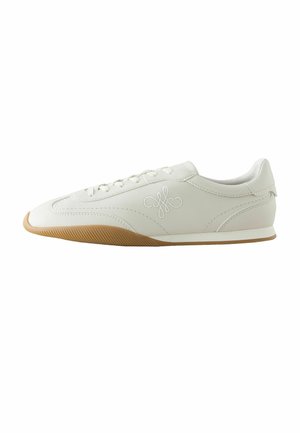 White low-top sneaker with brown rubber sole, stitching details, lace-up front, and embroidered logo on the side.