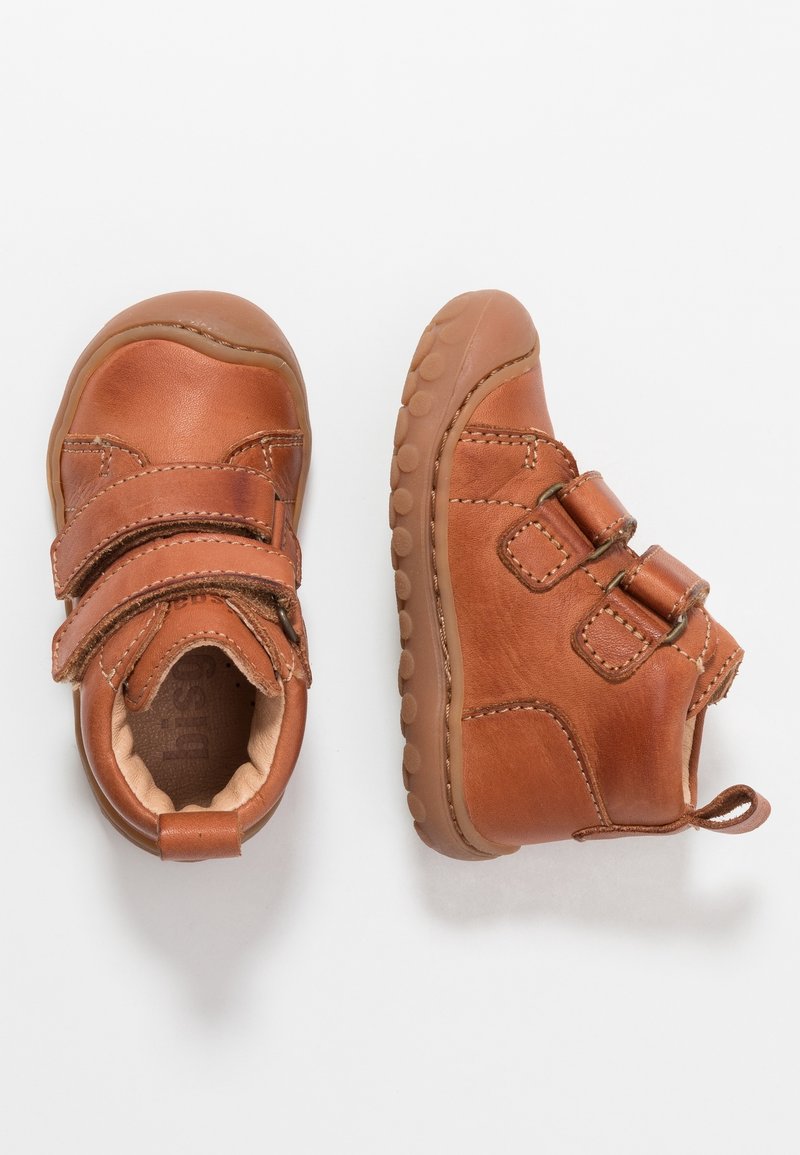 Chaussures pour tout-petit en cuir marron avec deux brides à velcro, bout rond et semelle en caoutchouc avec motifs antidérapants. Détails de couture sur les côtés.