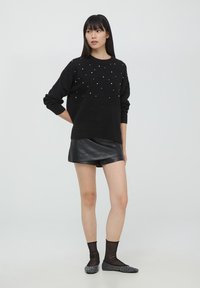Maglione nero a maglia con dettagli in perle, vestibilità rilassata e maniche lunghe; abbinato a una mini gonna in pelle nera e ballerine con fantasia.