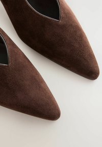 Rudos suedinės, smailianosiai bateliai su išpjovomis šonuose, kurie pasižymi lygiu текстūra ir elegantiška siluetu.