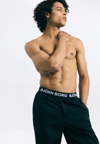 Fekete rövidnadrág széles, gumis derékrésszel, rajta fehér "BJÖRN BORG" márkanevével. Simaság jellemzi, térdhosszú fazon, zsebek nélkül.