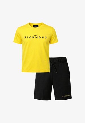 T-shirt gialla a maniche corte con la scritta "John Richmond" abbinata a pantaloncini neri con coulisse e piccolo logo coordinato sulla gamba sinistra.