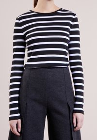 Svart och vitrandig långärmad topp i mjukt tyg, ihopparad med högmidjade mörkgrå vida byxor med sidospalter.