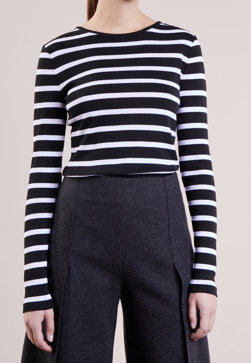 Svart och vitrandig långärmad topp i mjukt tyg, ihopparad med högmidjade mörkgrå vida byxor med sidospalter.