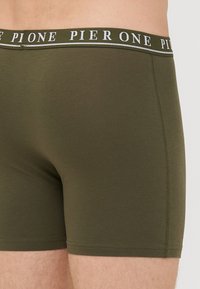 Boxers en vert olive en tissu doux. Comprend une ceinture élastique de marque contrastante et un ajustement serré avec des coutures plates.