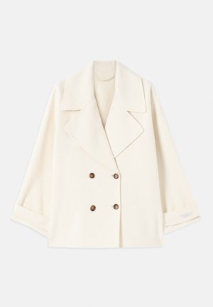 Manteau cropped de couleur crème à double boutonnage avec de larges revers et des boutons marron, présenté à plat avec les manches légèrement pliées.