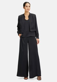 Zwarte satijnen twee-delige set bestaande uit een cropped bomberjack en wijde pants. Gladde textuur. Geen patronen of hardware-details zichtbaar.