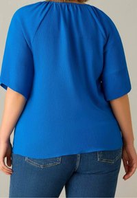 Blå texturerad topp med en avslappnad passform, korta ärmar och en rynkad halsringning; tillsammans med mid-rise blå jeans.