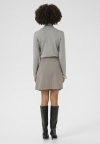Grauer Rollkragenpullover kombiniert mit einem braunen karottenförmigen Minirock und schwarzen kniehohen Stiefeln. Glattes Material, taillierte Passform und geometrisches Muster.
