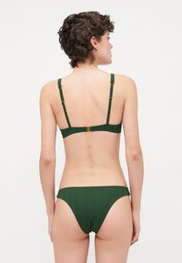 Grön ribbad bikini set med justerbara axelband och detaljer i guldfärgad metall. Toppen har en bakknäppning och trosorna har en måttlig skärning.