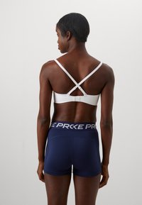 Vit sport-BH med korsade band och marinblå shorts med en bred midja med texten "PRKE". Slät tygkvalitet med en figurnära design.