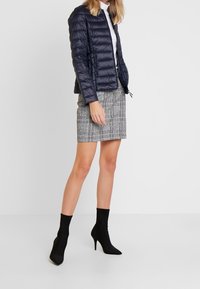 Doudoune marine à motif matelassé vertical, associée à une jupe mini pied-de-poule grise et bleue, et des bottines à talons aiguilles noires.