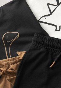 Pantalons et chemises noirs et marron pour enfants avec des dessins simples de dinosaures souriants en contours noirs et marron.