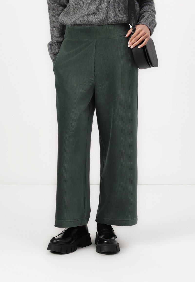 Pantaloni larghi in velluto a coste verde con una texture liscia, dotati di tasche laterali e un fit rilassato. Abbinati a mocassini neri chunky.
