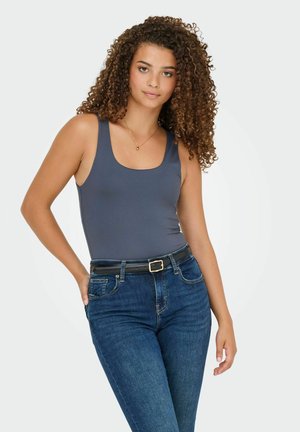 Grauer ärmelloser Body mit runder Ausschnittlinie, kombiniert mit dunkelblauen hochtaillierten Jeans und einem schwarzen Gürtel, vor einem hellen Hintergrund.