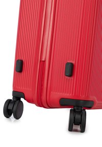 Valigia rigida rossa con superficie texturizzata, accessori neri, chiusura con zip e doppie ruote girevoli per la mobilità.