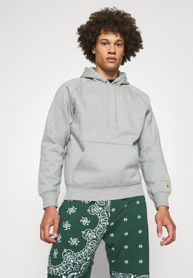 Sudadera gris hecha de tejido suave, con un bolsillo canguro, capucha con cordón y puños acanalados, combinada con pantalones verdes con estampado.