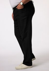 Pantalons en denim noir à coupe droite, avec poches latérales et texture lisse, accompagnés de baskets blanches.
