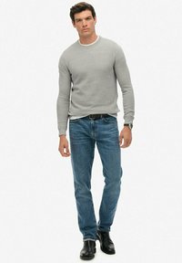 Szary sweter z dzianiny, niebieskie dżinsy, czarne skórzane buty. Dopasowany krój z długim rękawem, okrągłym dekoltem i teksturowanym materiałem.