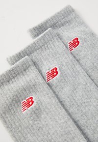 Drei Paar hellgraue Baumwollsocken mit gerippten Bündchen, jeweils mit einem roten Logo auf jeder Socke. Die Textur ist weich und gestrickt.