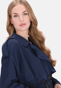 Donkerblauwe trenchcoat met een brede kraag en knoopsluiting aan de voorkant. Voorzien van een getailleerde tailleband en een zachte stoftextuur.