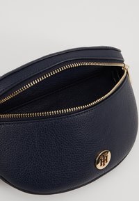 Borsa a pochette in pelle blu navy con una finitura testurizzata, dettagli in zip dorata e un accento circolare con logo dorato sul davanti. L'apertura superiore rivela un interno spazioso.