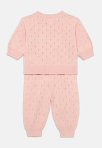 Conjunto de punto rosa de dos piezas que incluye una blusa de mangas cortas y pantalones ajustados, con un patrón de pequeños agujeros en forma de diamante y puños acanalados.