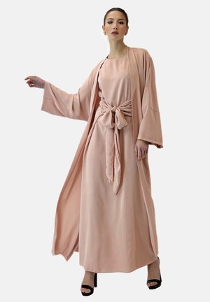 Vestido largo de color rosa claro con un lazo en la cintura, mangas anchas y una silueta fluida. Textura de tela suave y caída elegante. Sandalias de tacón alto.